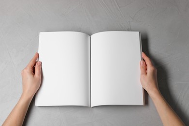 Woman holding open notebook with blank pages at light grey table, top view. Mockup for design