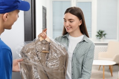 Dry-cleaning delivery. Courier giving jacket in plastic bag to woman indoors