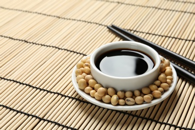 Photo of Dish of soy sauce with beans and chopsticks on bamboo mat. Space for text