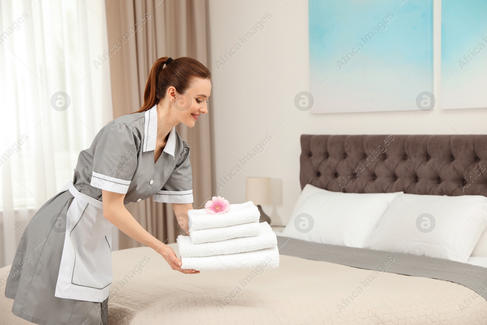 Photo of Chambermaid putting fresh towels on bed in hotel room. Space for text