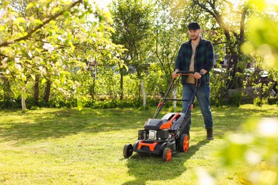 Photo of Man cutting green grass with lawn mower in garden