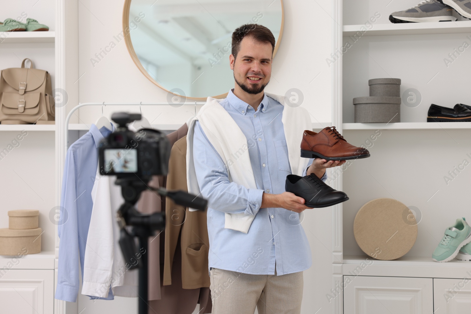 Photo of Smiling fashion blogger showing shoes while recording video at home