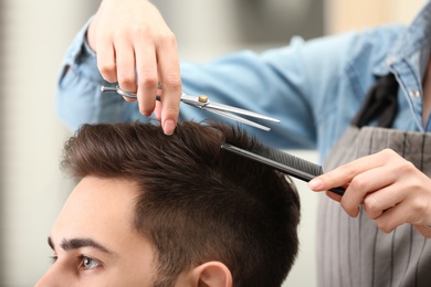 Barber making stylish haircut with professional scissors in beauty salon, closeup