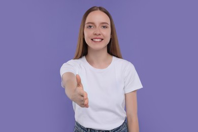 Photo of Happy young woman welcoming and offering handshake on purple background