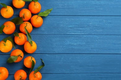 Fresh ripe tangerines with green leaves on blue wooden table, flat lay. Space for text