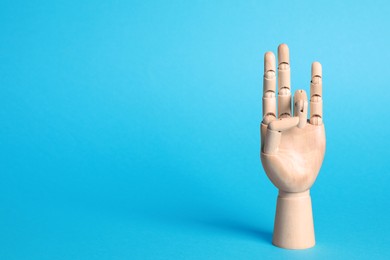 Photo of Wooden mannequin hand on light blue background. Space for text