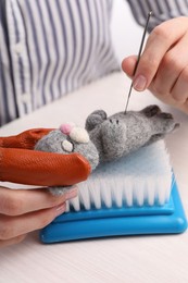 Photo of Woman felting toy cat from wool at light wooden table, closeup