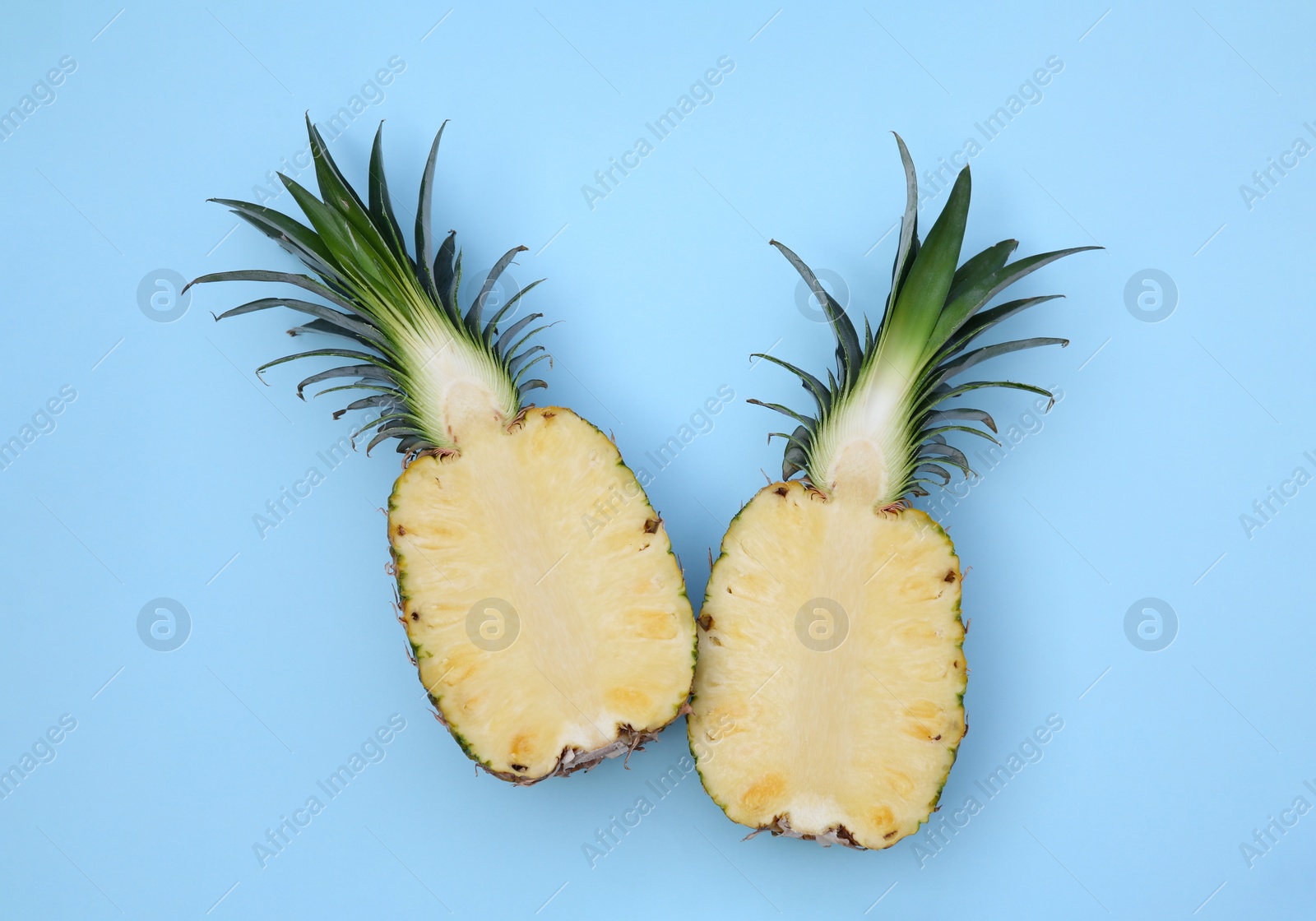 Photo of Halves of ripe pineapple on light blue background, flat lay