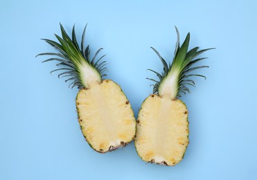 Photo of Halves of ripe pineapple on light blue background, flat lay