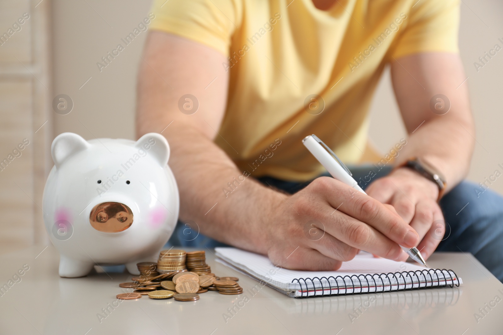 Photo of Man with notebook, piggy bank and money at table indoors, closeup