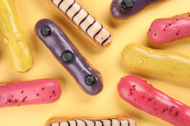 Delicious eclairs covered with glaze on yellow background, flat lay