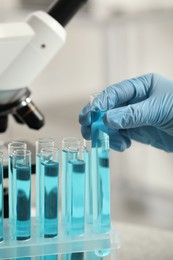 Photo of Scientist taking test tube with light blue liquid in laboratory, closeup