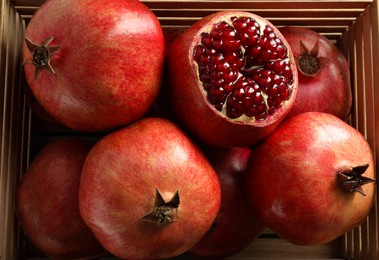 Photo of Ripe pomegranates in wooden crate, top view