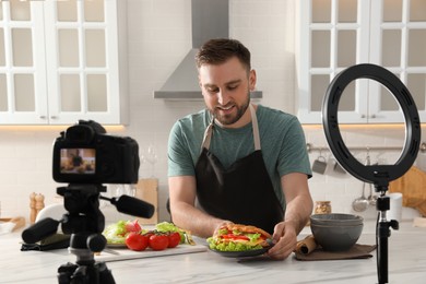 Blogger with tasty croissant recording video in kitchen at home. Using ring lamp and camera