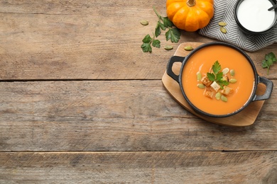 Photo of Tasty creamy pumpkin soup with croutons, seeds and parsley in bowl on wooden table, flat lay. Space for text