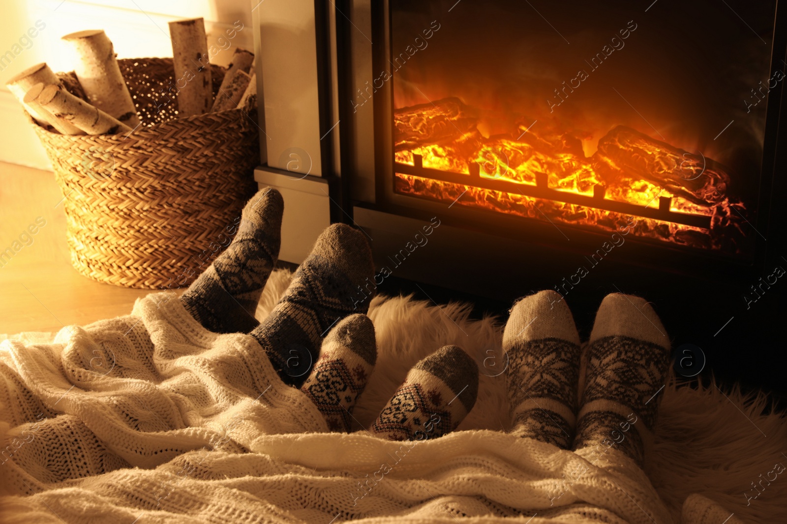 Photo of Family in warm socks resting near fireplace at home, closeup of legs