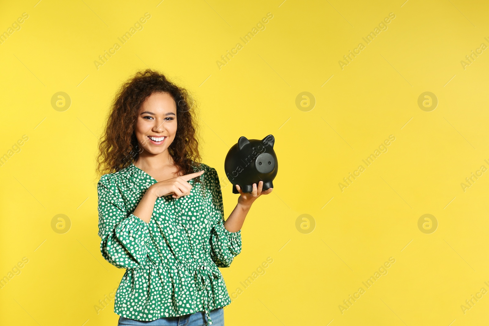 Photo of Young African-American woman with piggy bank on color background, space for text. Money saving