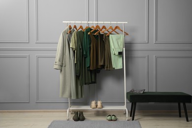 Photo of Rack with different stylish women`s clothes, shoes and bag on bench near grey wall indoors