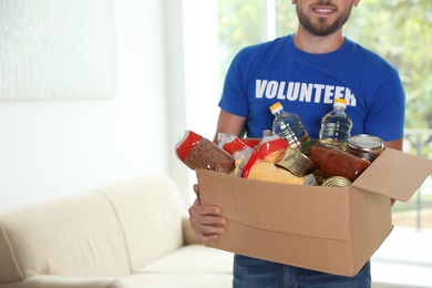 Photo of Male volunteer holding box with donations indoors. Space for text