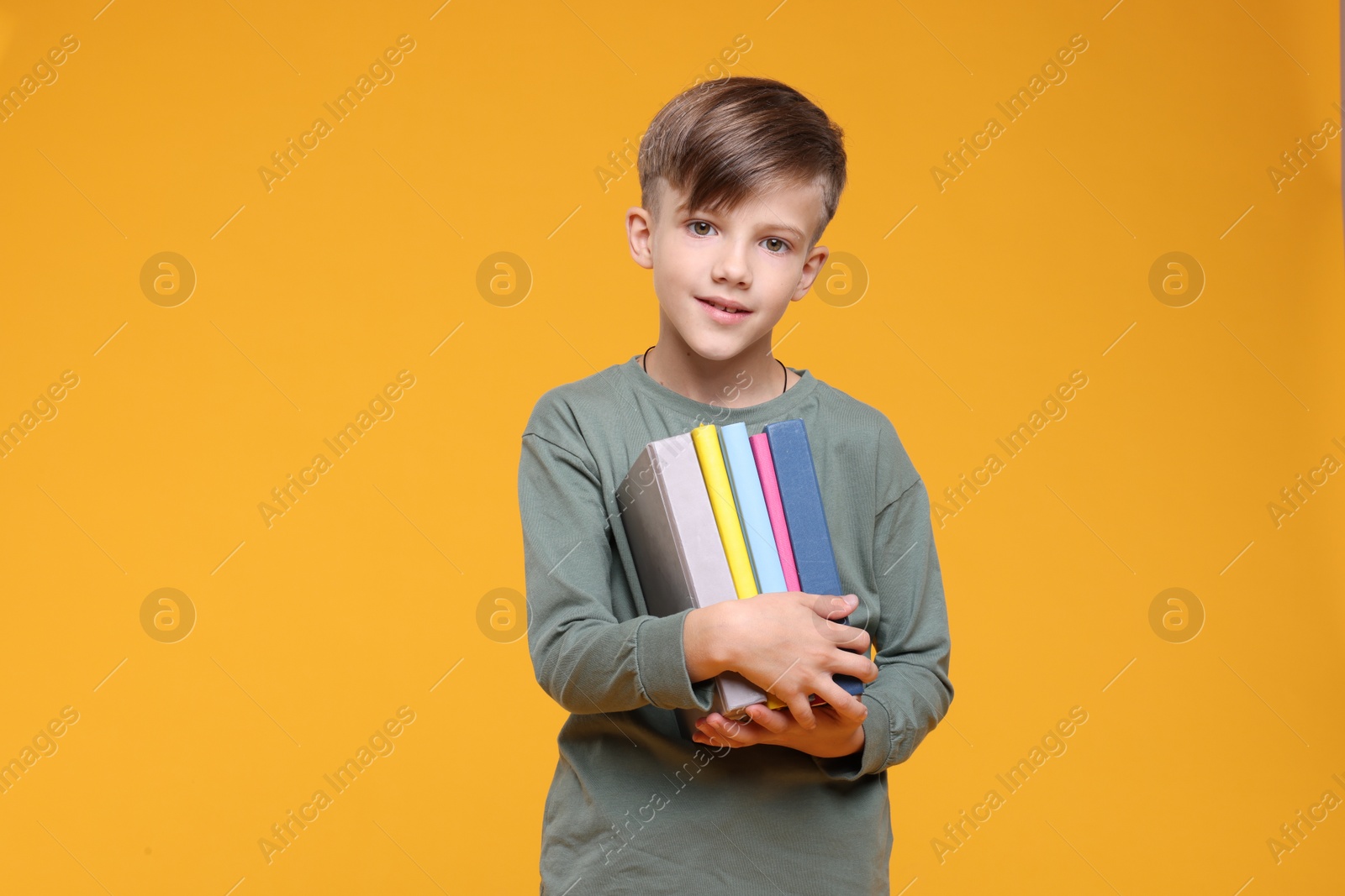 Photo of Cute schoolboy with books on orange background