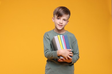 Photo of Cute schoolboy with books on orange background