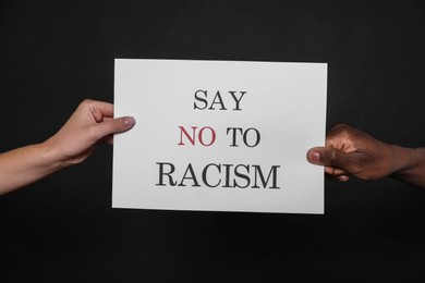 Photo of Woman and African American man holding sign with phrase Say No To Racism on black background, closeup