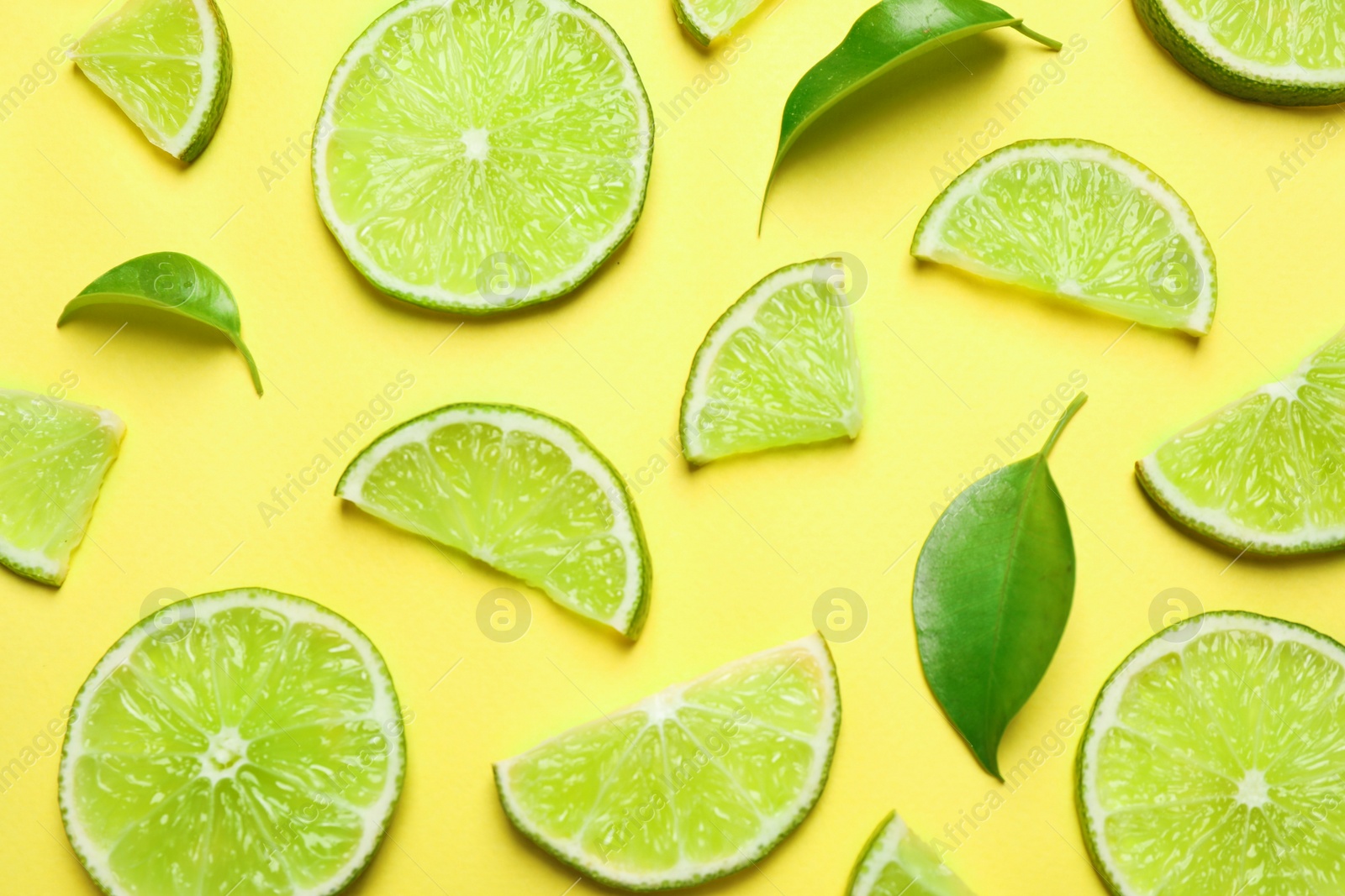 Photo of Juicy fresh lime slices and green leaves on yellow background, flat lay