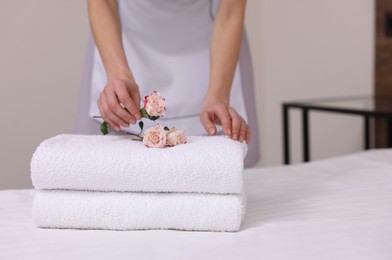 Photo of Chambermaid putting flowers on fresh towels in hotel room, closeup