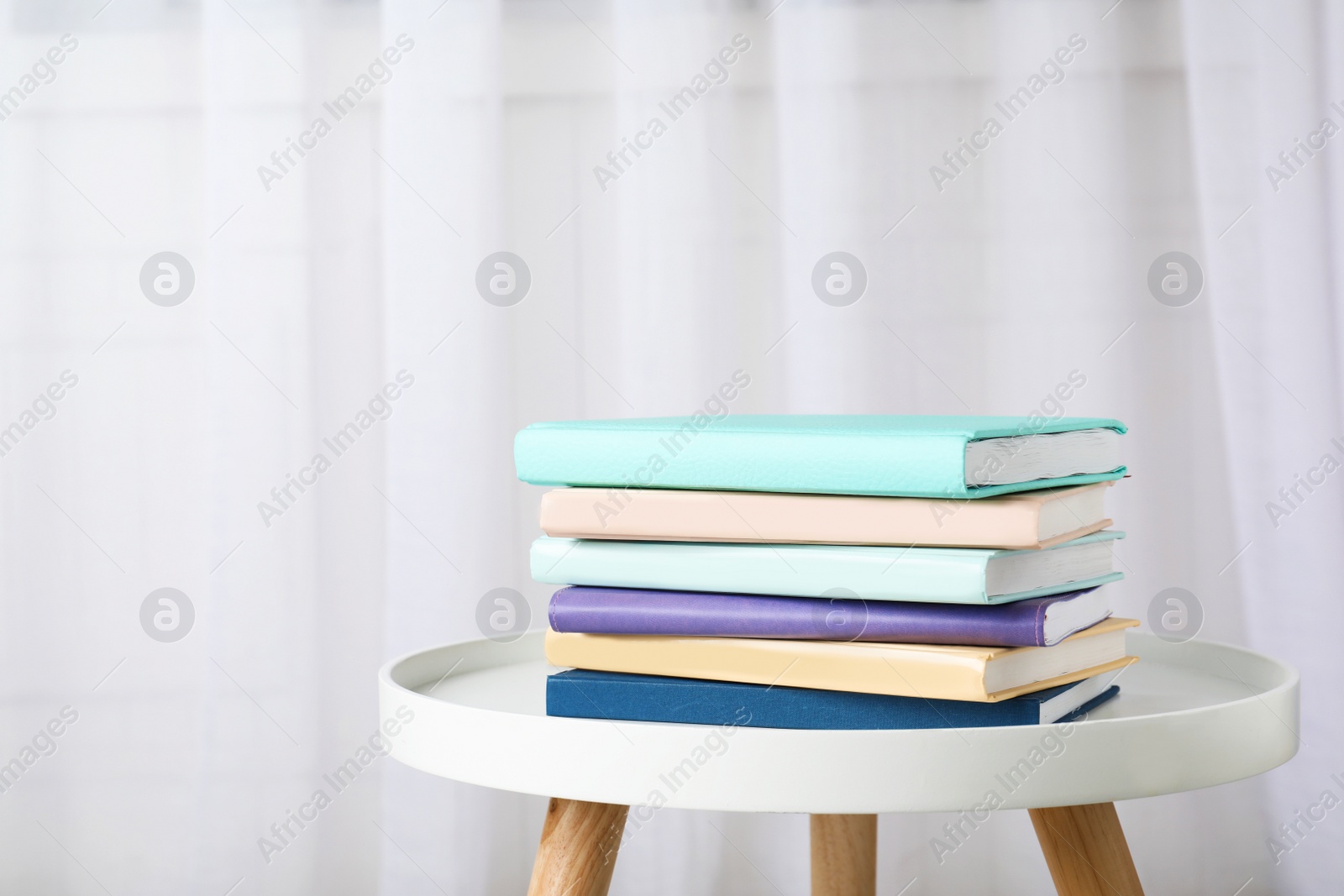 Photo of Stack of books on table against curtain. Space for text