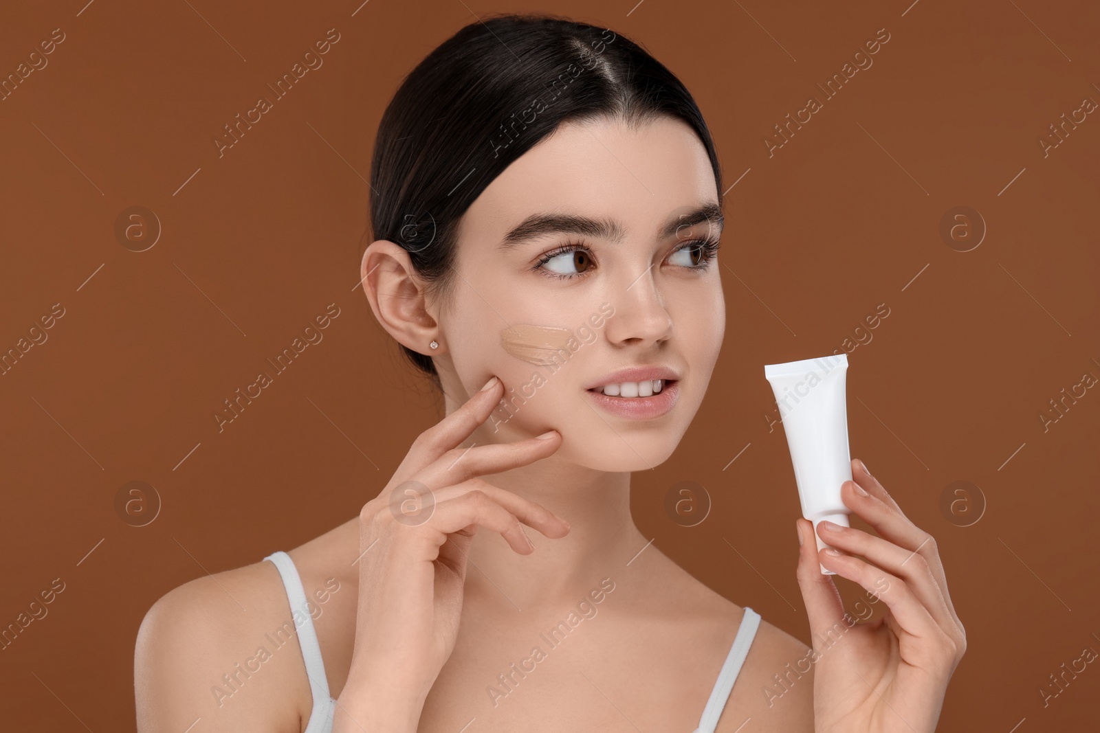 Photo of Teenage girl holding tube with foundation on brown background
