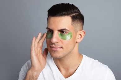 Photo of Man applying green under eye patch on grey background