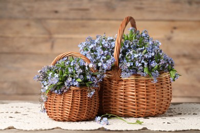 Photo of Beautiful forget-me-not flowers in wicker baskets on wooden table, closeup