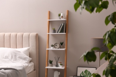 Stylish bedroom interior with decorative ladder and plants near grey wall