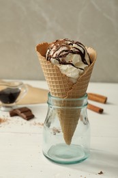 Photo of Delicious vanilla ice cream with toppings in wafer cone on white wooden table