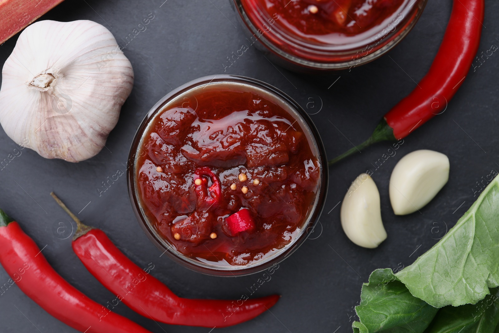 Photo of Tasty rhubarb sauce and ingredients on black table, flat lay