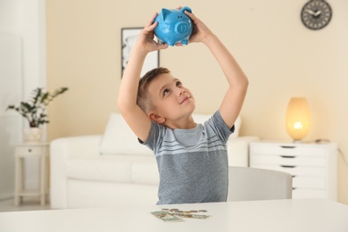 Photo of Curious little boy with piggy bank indoors