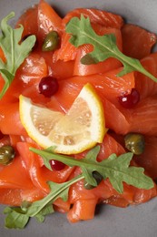 Photo of Salmon carpaccio with capers, cranberries, arugula and lemon on plate, top view