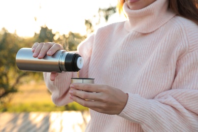 Woman pouring hot drink from thermos into cap outdoors, closeup