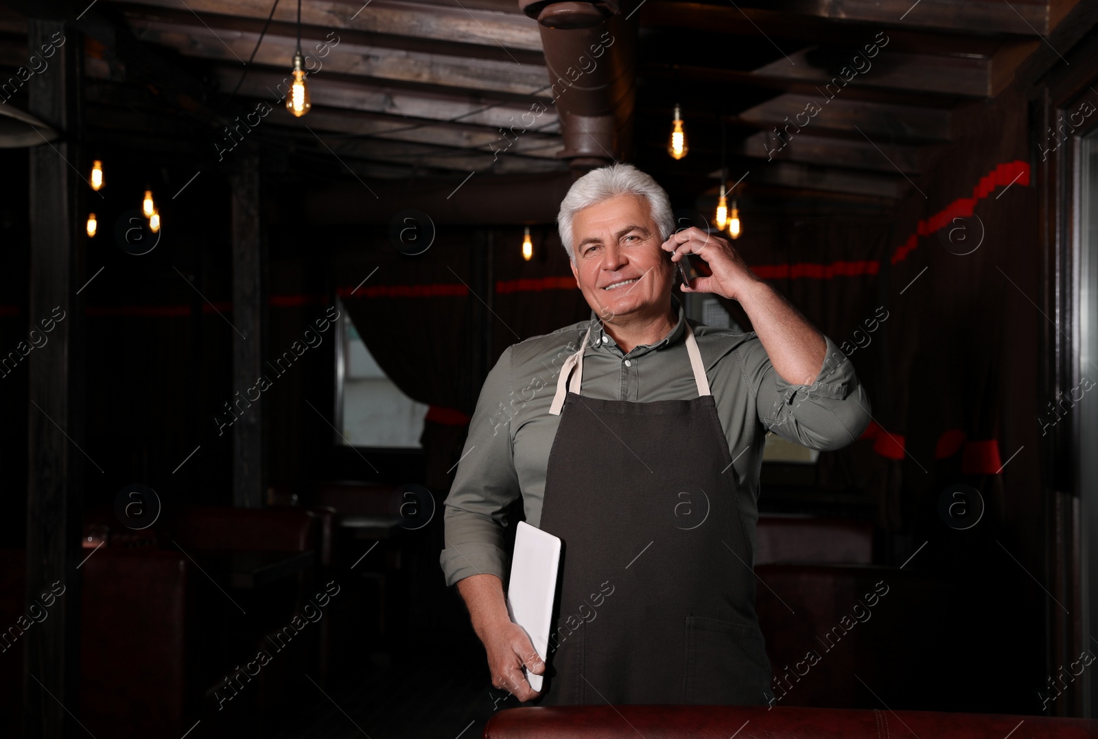 Photo of Senior business owner talking on phone in his restaurant