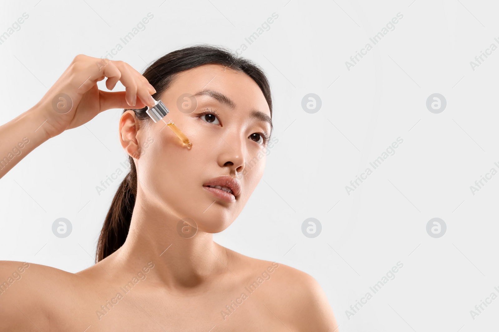 Photo of Beautiful young woman applying cosmetic serum onto her face on white background, space for text