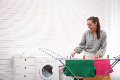 Photo of Young woman hanging clean laundry on drying rack indoors