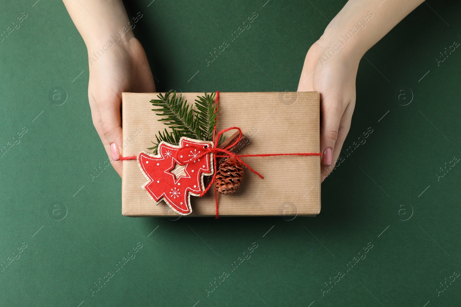 Photo of Woman holding beautifully wrapped Christmas gift box on dark green background, top view