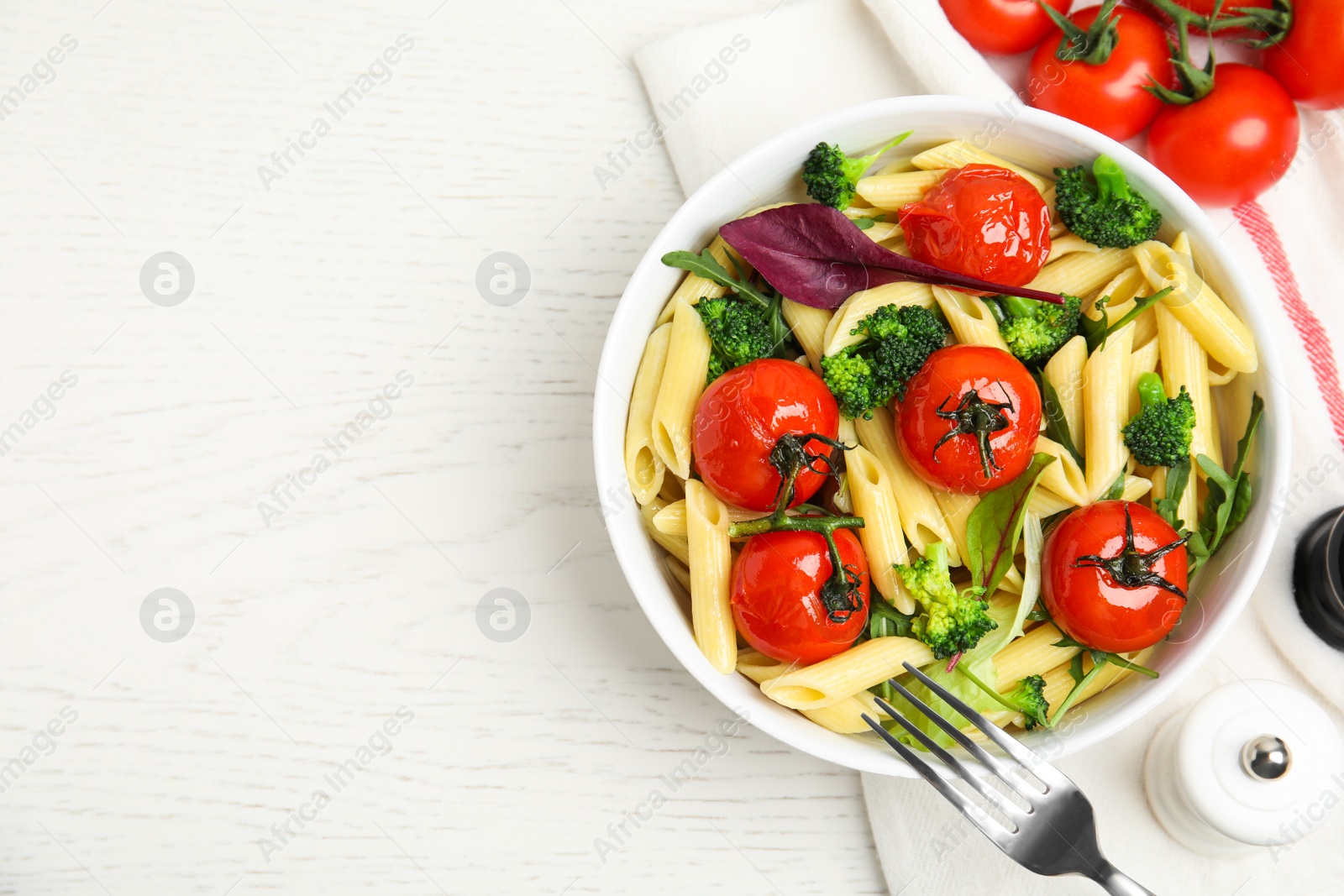 Photo of Bowl of delicious pasta with tomatoes, arugula and broccoli on white wooden table, flat lay. Space for text