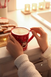 Woman holding cup with hot drink in kitchen, closeup