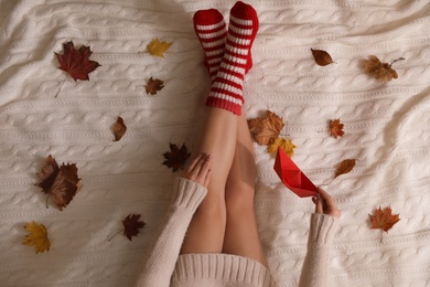 Photo of Woman in warm socks with dry leaves on knitted blanket, top view