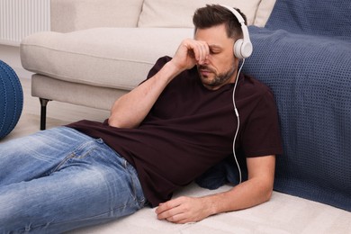 Upset man listening to music through headphones while lying on floor at home. Loneliness concept