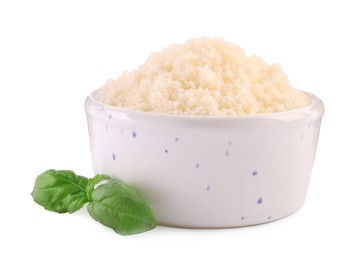 Delicious grated parmesan cheese in bowl and basil on white background