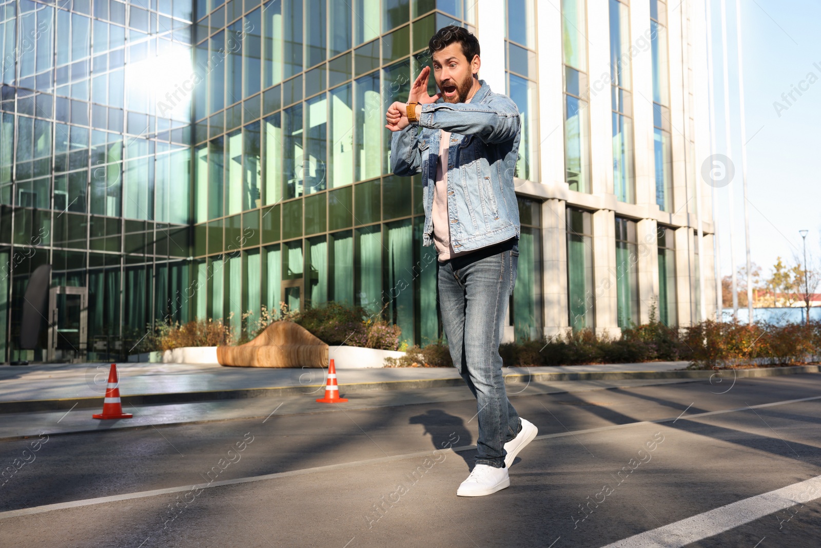 Photo of Emotional man checking time on watch near building. Being late concept