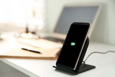 Photo of Mobile phone with wireless charger on white table. Modern workplace accessory