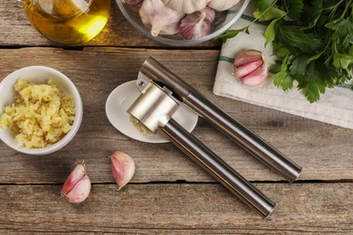 Garlic press and products on wooden table, flat lay